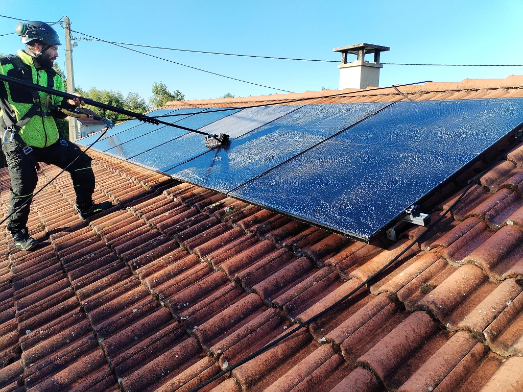Technicien nettoyant des panneaux solaires avec une perche sur un toit en tuiles