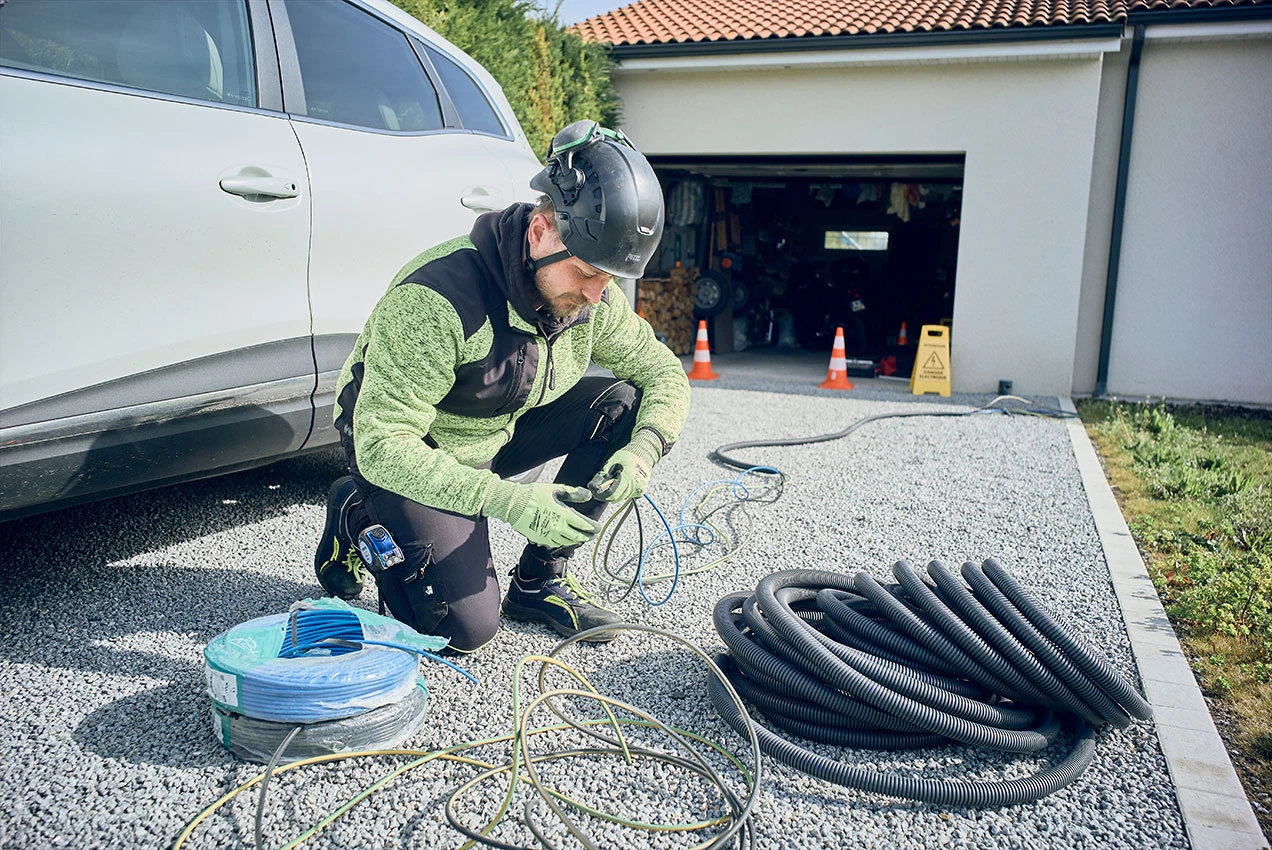 Technicien EV Auvergne préparant le câblage d’une borne de recharge devant un garage