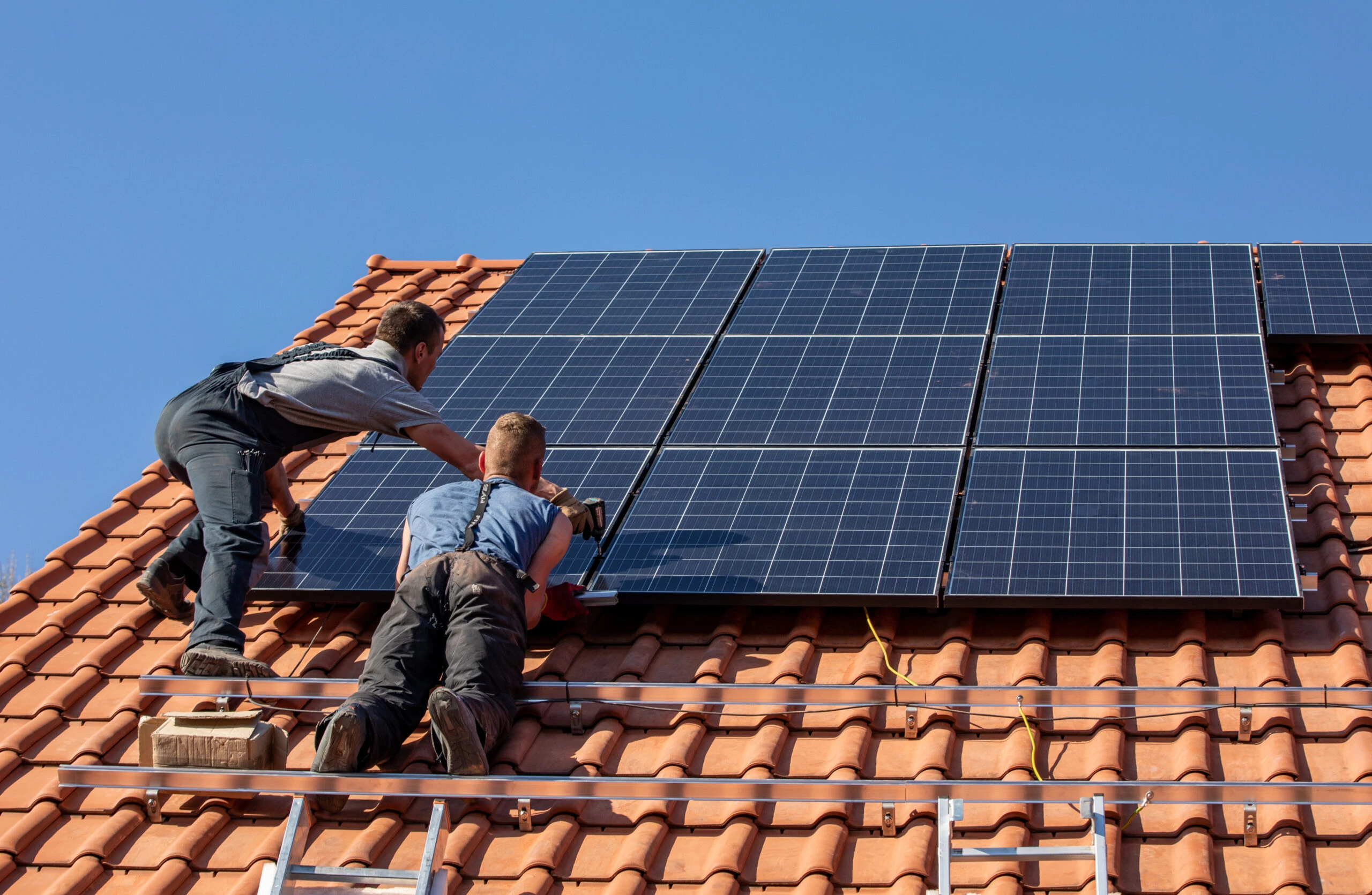 Pose de panneaux solaires sur une toiture en tuiles par deux techniciens EV Auvergne