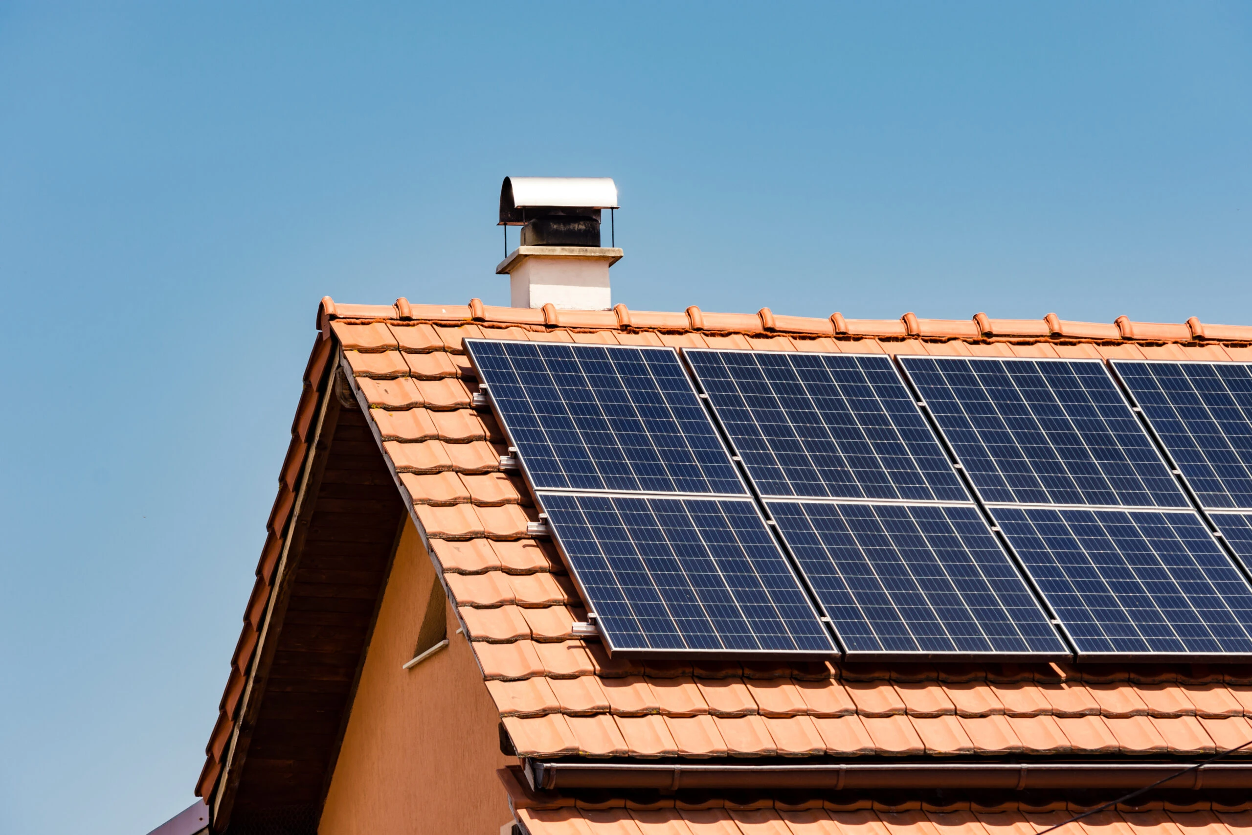 Panneaux solaires noirs posés sur une toiture en tuiles avec cheminée